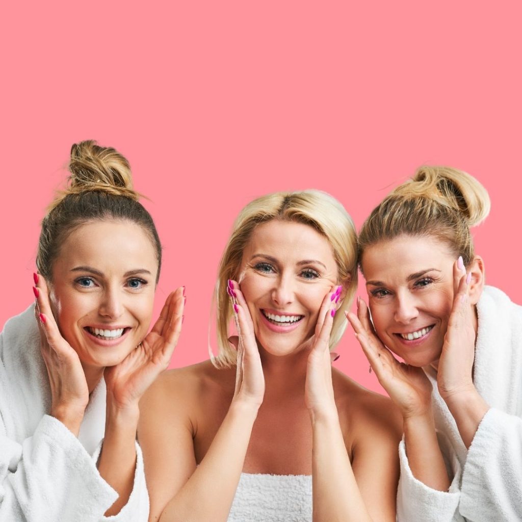 Three women, between the ages of 30-60, looking happy, in bathrobes, taking care of their skin. 