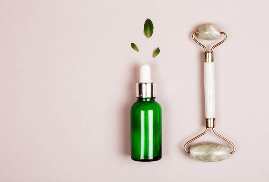  Bottle of serum and face roller with light pink background.