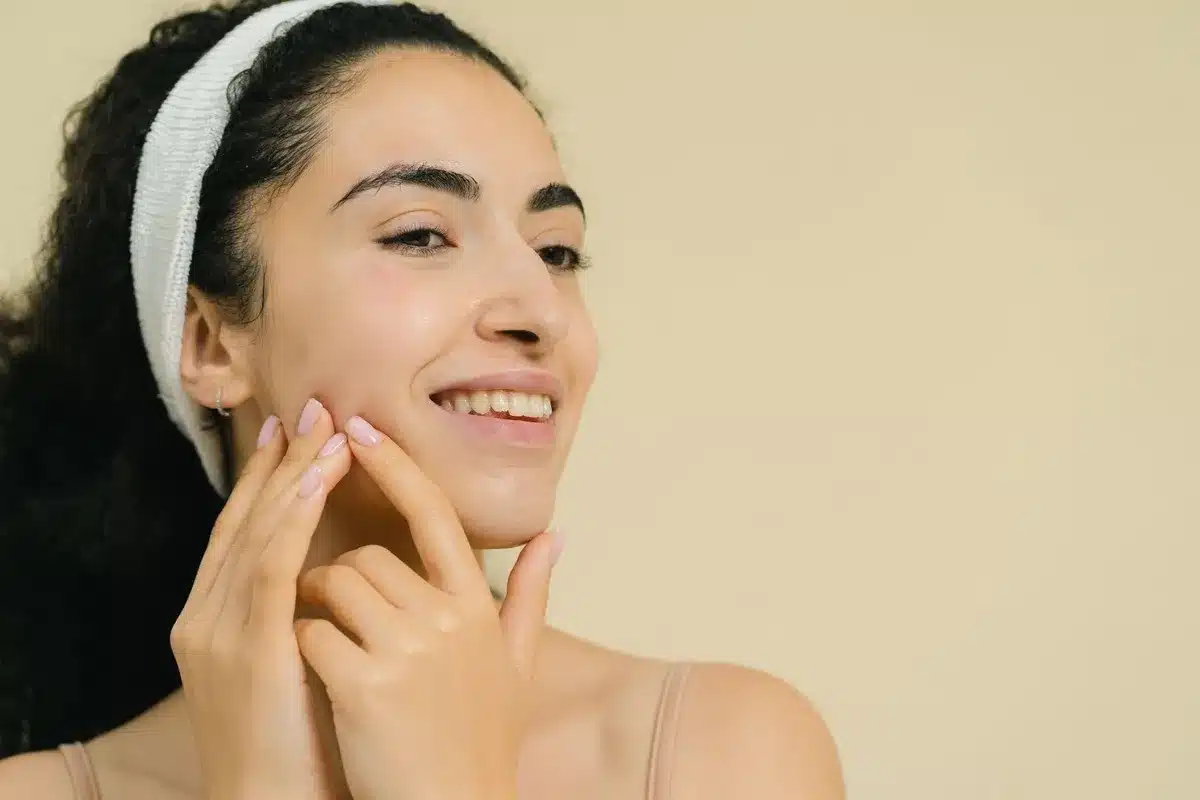 A smiling woman applies a skin treatment, highlighting natural beauty and the benefits of microcurrent facials.